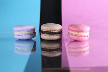 Three macaroons on a blue black pink background different colors different tastes with place for text and reflection.の写真素材