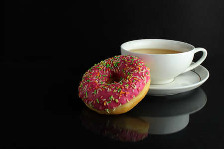 Donut with pink icing berliner lies next to a cup of coffee tea delicious breakfast snack day without diet on black background copyspace.の写真素材