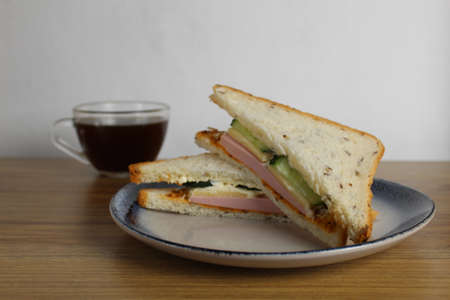 Breakfast snack lunch sandwich with sausage ham cheese cucumber lies on a plate next to a cup of tea or coffee. Morning serve. preparation. Cafe Restaurant.の写真素材