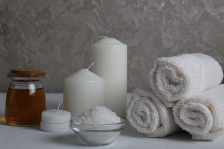 Spa relax massage home care for soy body. White candles towels oil in a jar bottle scrub on a white gray background with space for text. Beauty parlor.の写真素材