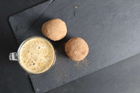 coffee with dessert cup with coffee with foam and next to them are chocolate cakes with cocoa on a black stone background with a place for text. breakfast.の写真素材