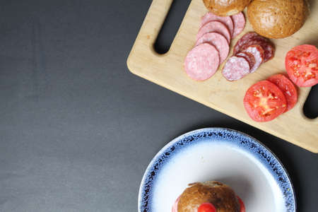 cooking a sandwich vegetables and sausage bun rye lie on a board tray made of wood on a black background. view from above. breakfast lunch snack.の写真素材