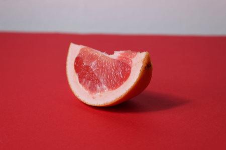 a piece of a slice of red grapefruit on a red background with a hard shadow. Fruit creative benefit...