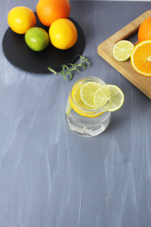 Still life: citrus lemonade of lemons, orange, lime in a glass of fruit on a tray on a gray...
