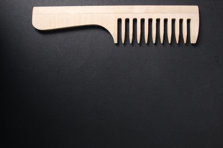 Concept of selection of tools for hair care. Wooden natural comb on black background. Hair...