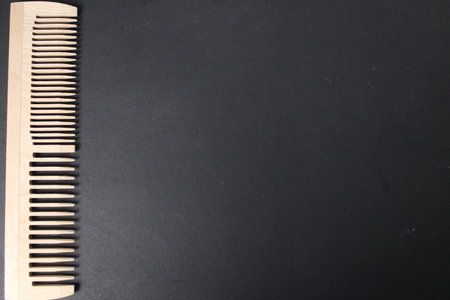 The concept of using natural materials in everyday life. Natural wood comb on black background with...