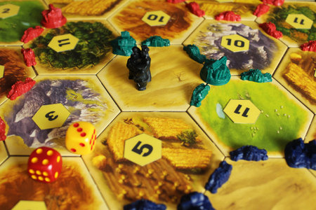 A catan board game, the green and blue tiles of the players are displayed on the field next to the...