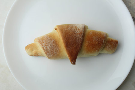baked toasty bristleside croissant on a white plate close-up top view.
