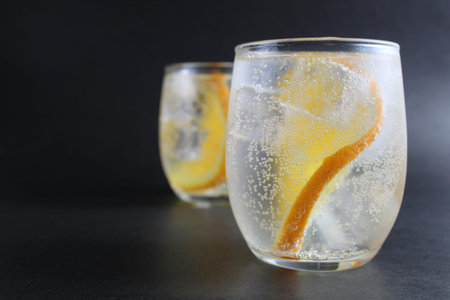 lemonade with orange and ice in a glass on a black background next to lies ice and orange. Summer...