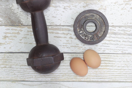Dumbbells and eggs on a wooden background. Top view