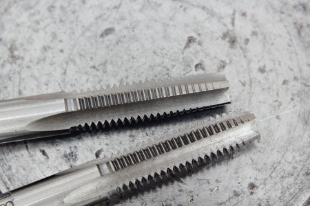Metal thread tap tool on metal background. Close-up.