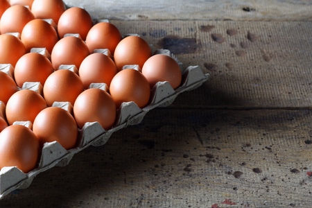 Fresh raw chicken eggs in carton egg box on wooden backgroundの写真素材