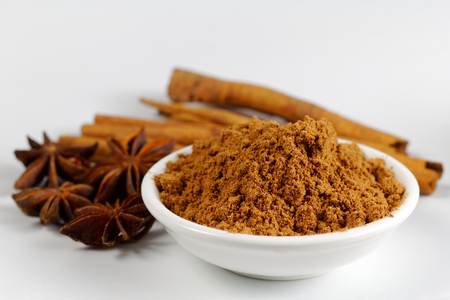 Chinese Five-Spice powder in a bowl with cinnamon and star anise on white paperの写真素材