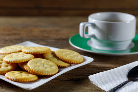 Round cracker on white plate and coffee cup on wood background