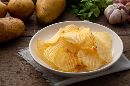 Fried wavy potato chips snack in white plate on wooden table