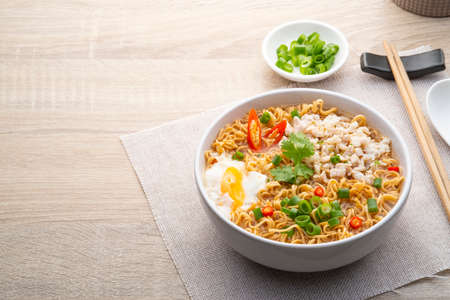 Instant noodle soup with minced pork and boiled egg in white bowl on wood table.with copy spaceの写真素材