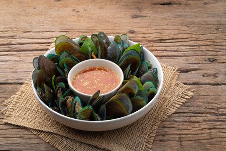 Steamed mussels on white plate with Thai seafood dipping sauce on wooden plate