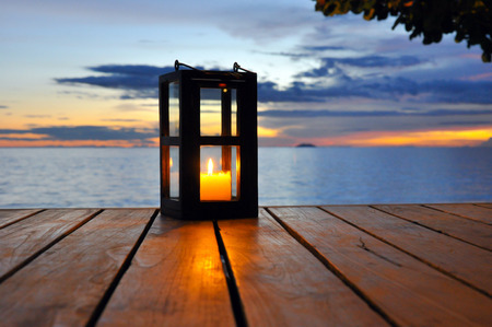 Candle lantern on wooden table with twilight sea backgroundの写真素材