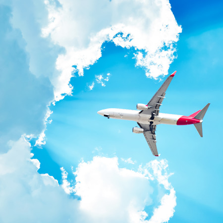 Airplane flying in sunny sky with cloudsの写真素材