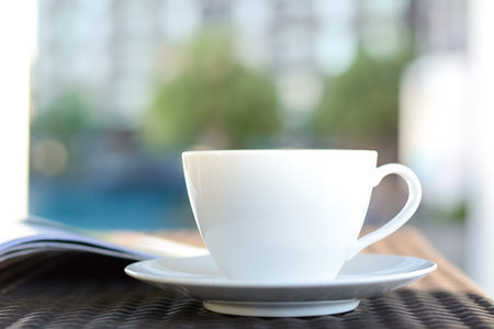 Coffee cup with book on the table in blurred building & green plant background - chill out in resort or hotel conceptの写真素材