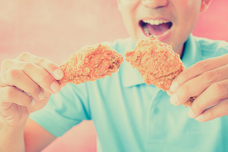 A man with opening mouth about to eat deep fried chicken legs or drumsticks -vintage (retro) style color effectの写真素材
