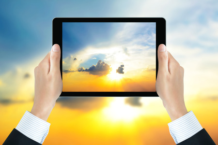 Businessman hands holding tablet pc, taking picture of the sun shining in the sky - bright business conceptの写真素材