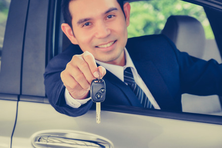 Asian businessman giving a car key, car sale, rental & insurance concepts - vintage style color with soft focusの写真素材