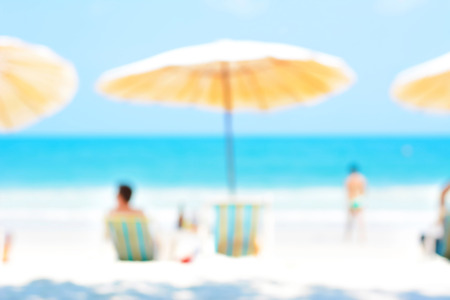 Blurred blue sea and white sand beach with parasols, beach chairs and some people - holiday and vocation background conceptの写真素材