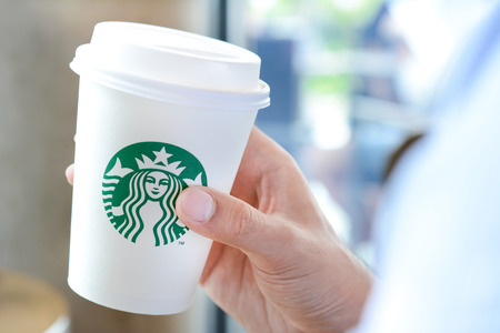 Hand holding Starbucks coffee cup with brand logo. Starbucks brand is worldwide coffeehouse chains from USA.のeditorial素材