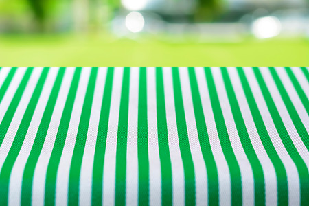 Table top covered with striped tablecloth on blurred green yard background - can be used for montage or display your productsの写真素材