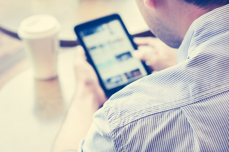 A man using tablet pc (blurred screen) in coffee shop with coffee cup on the table - vintage tone, soft focusの写真素材