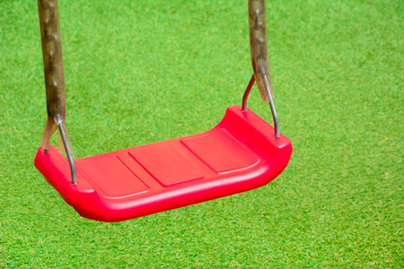 Red swing on green lawn background
