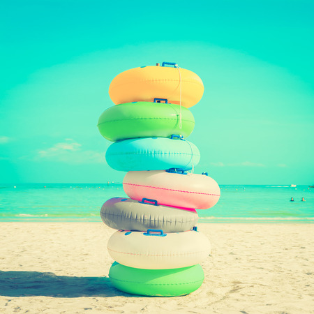 Stack of colorful rubber rings (or swim rings) on white sand beach, vintange tone - summer holiday conceptの写真素材