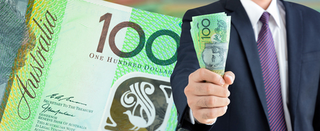 Businessman holding money, Australian dollars (AUD), on 100 banknote background  - financial and investment panorama background conceptの写真素材