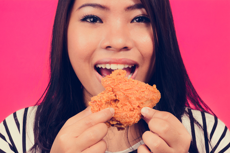 Young Asian woman eating fried chicken on colorful pink background, vintage toneの写真素材