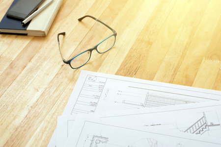 Architectural blueprints, eyeglasses, book and some equipments on wooden table