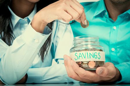 Woman hand putting money (coin) in the glass jar labeled SAVINGS held by a manの写真素材