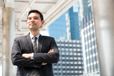 Asian businessman standing and crossing his arms in blur building backgroundの写真素材