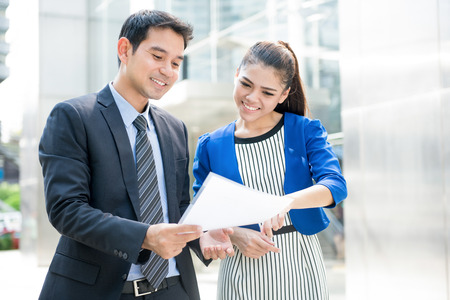 Business people discussing document while walking outdoors in front of office buildingの写真素材
