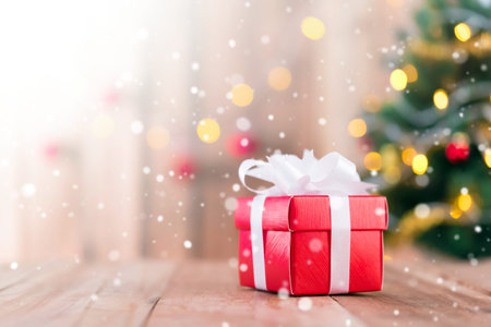 Red gift box on wood table top in Christmas tree bokeh background with snow