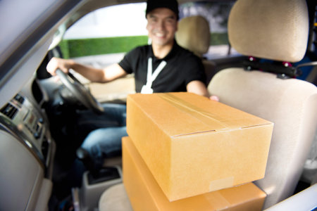 Delivery man giving postal package while sitting in car - courier and delivery service concepts