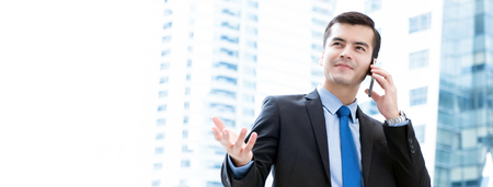 Businessman calling on smartphone with hand gesture in blur office building background - panoramic bannerの写真素材