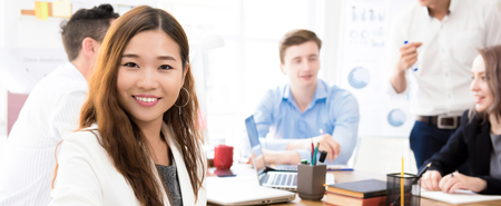 Smiling young confident Asian businesswoman at the office with her mixed race colleagues in background, panoramic bannerの写真素材
