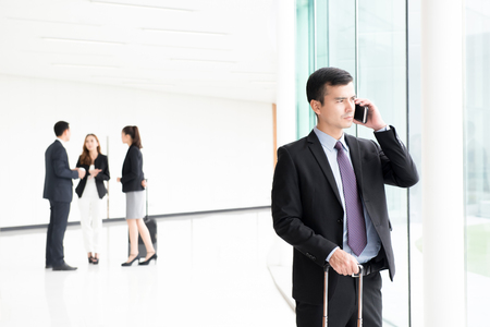 Traveling businessman calling on smartphone at building hallway (airport terminal)の写真素材