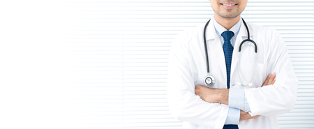 Smiling doctor standing and crossing his arms in white blind background, panoramic banner with copy spaceの写真素材