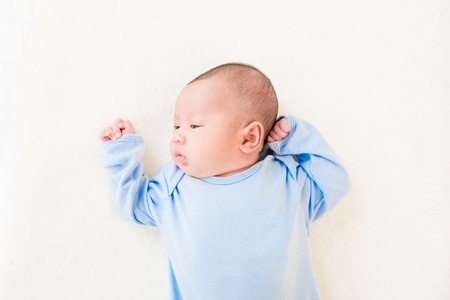 Cute newborn baby lying on white sheet - top view