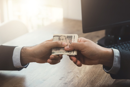 Businessman giving money, Japanese Yen banknotes, to his partner at working tableの写真素材
