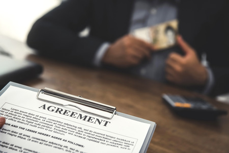Businessman putting money into his suit pocket while making an agreement - bribery and corruption conceptの写真素材