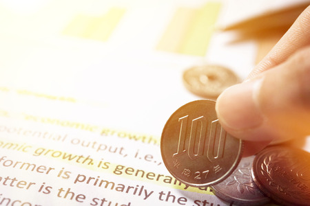 Hand picks up money, 100 Japanese yen coin, on economic report paperの写真素材