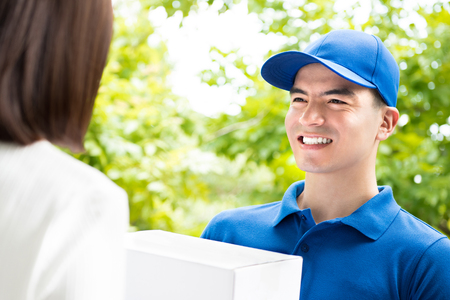 Smiling delivery man in blue uniform delivering parcel box to a woman - courier service conceptの写真素材